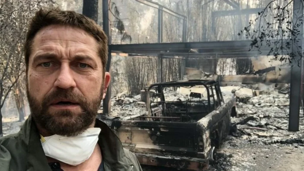 Gerard Butler in front of burned down house